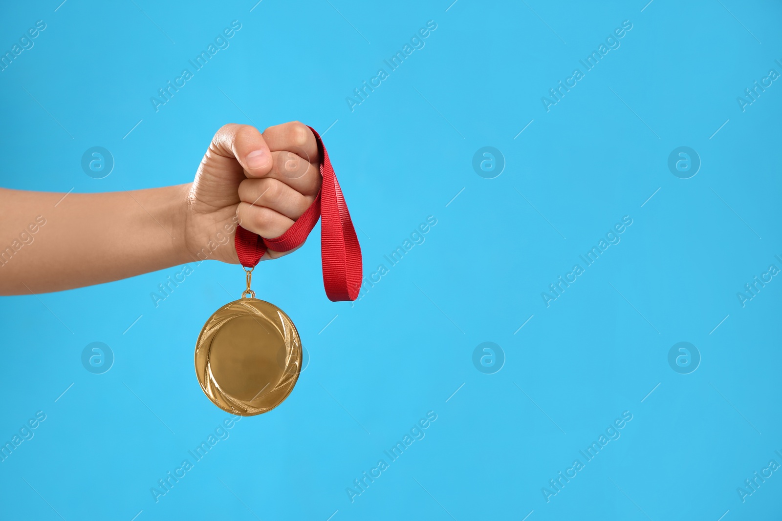 Photo of Woman holding gold medal on light blue background, closeup. Space for text