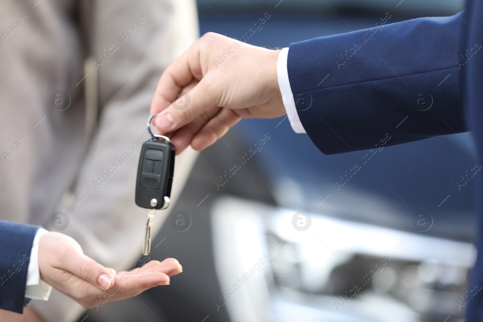 Photo of Salesman giving key to customers in modern auto dealership, closeup. Buying new car