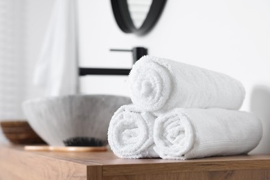 Photo of Rolled bath towels on wooden table in bathroom. Space for text