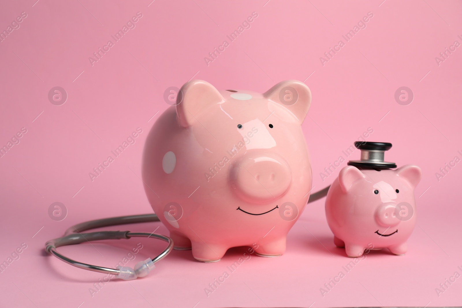 Photo of Two piggy banks and stethoscope on pink background. Medical insurance