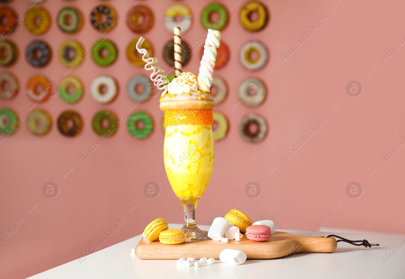 Photo of Tasty milk shake with sweets in glass and macarons served on table indoors
