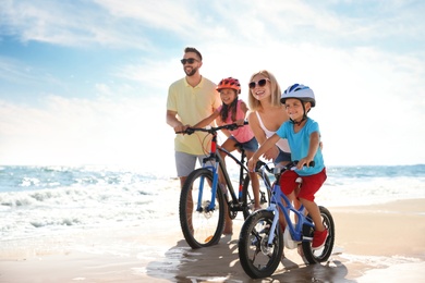 Photo of Happy parents teaching children to ride bicycles on sandy beach near sea