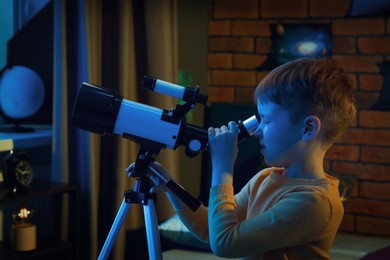 Little boy looking at stars through telescope in room