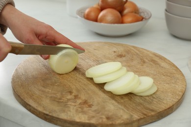 Photo of Woman cutting white onion into rings at countertop, closeup
