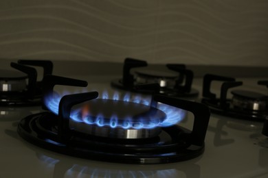 Photo of Modern gas cooktop with burning blue flame in kitchen