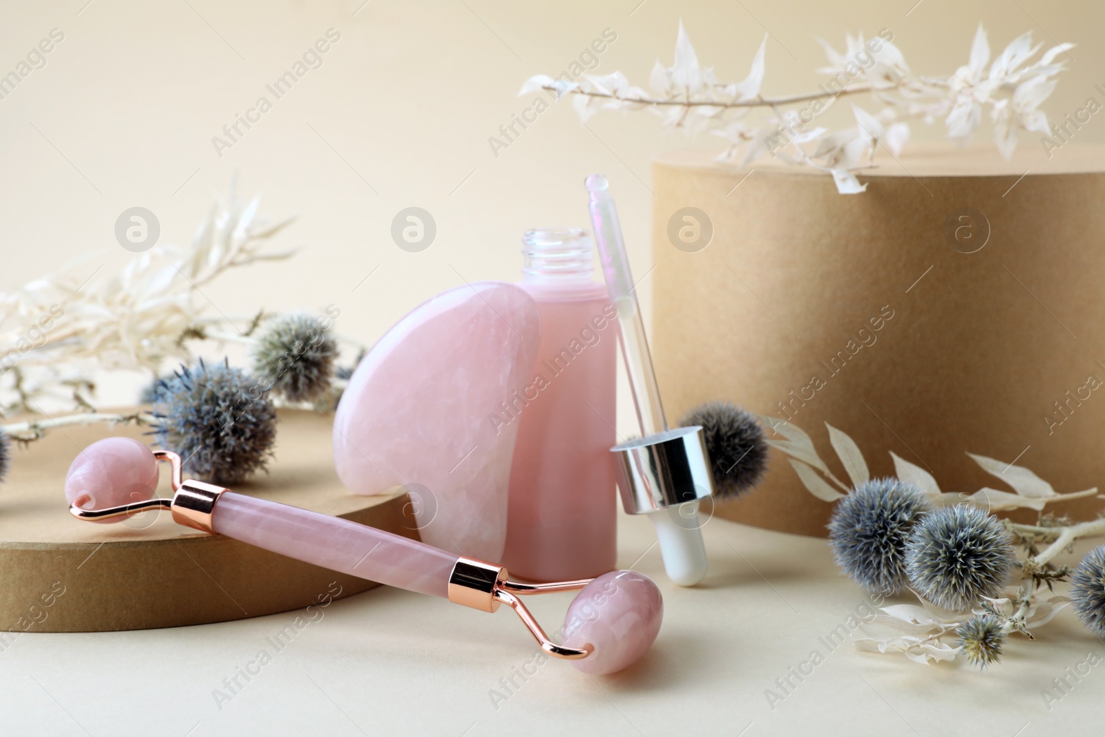 Photo of Composition with rose quartz gua sha tool, facial roller and bottle of serum on beige background