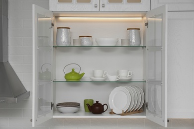 Photo of Open cabinet with different clean dishware in kitchen