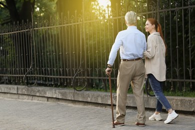 Photo of Senior man with walking cane and young woman outdoors, back view. Space for text