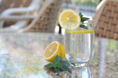 Refreshing water with lemon and mint on glass table in cafe, space for text