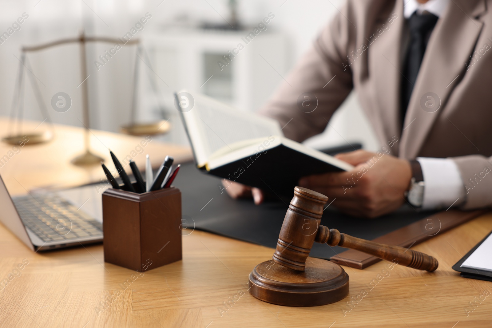 Photo of Lawyer reading book at table in office, focus on gavel