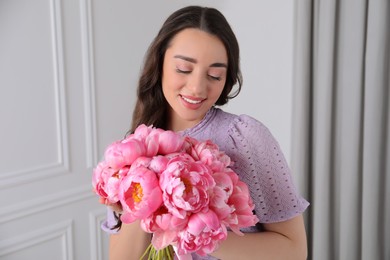 Beautiful young woman with bouquet of pink peonies indoors