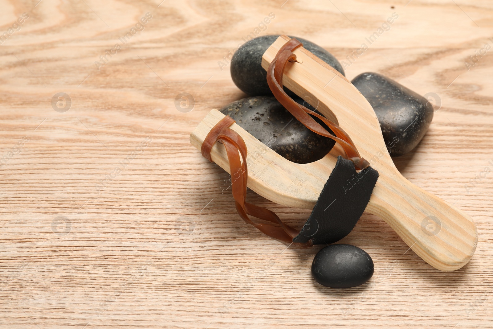 Photo of Slingshot with stones on wooden table, closeup. Space for text