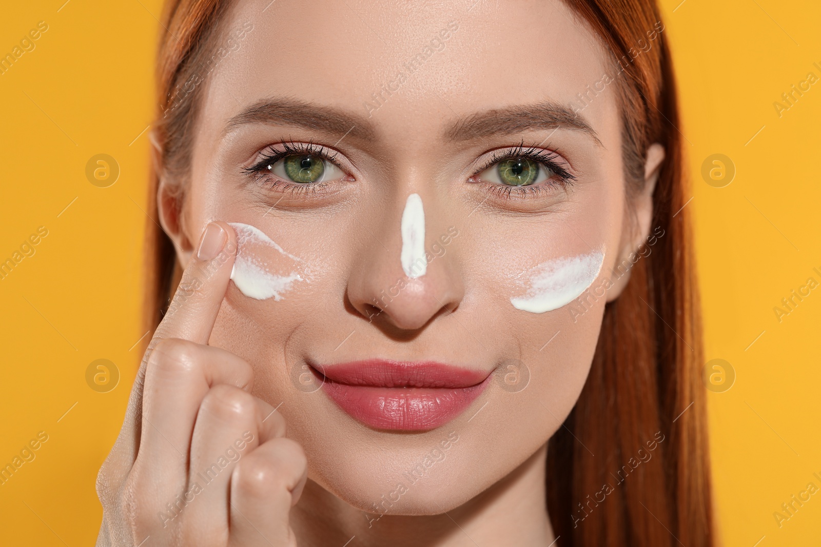 Photo of Beautiful young woman with sun protection cream on her face against orange background, closeup