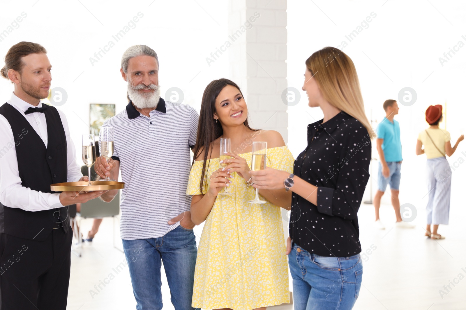 Photo of Waiter serving champagne to group of people at exhibition in art gallery