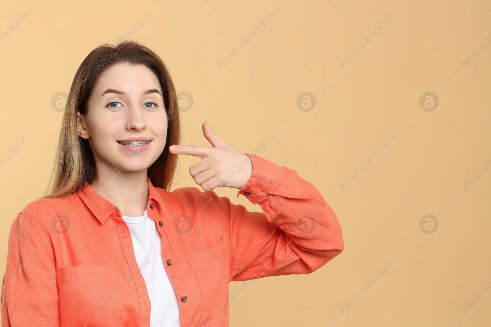 Photo of Portrait of smiling woman pointing at her dental braces on beige background. Space for text