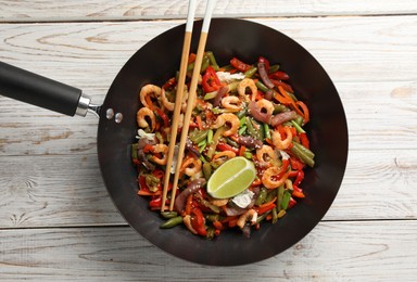 Shrimp stir fry with vegetables in wok and chopsticks on light wooden table, top view