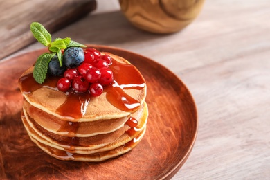 Stack of tasty pancakes with berries and syrup on table