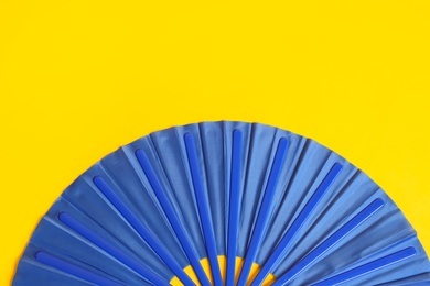 Blue hand fan on yellow background, top view