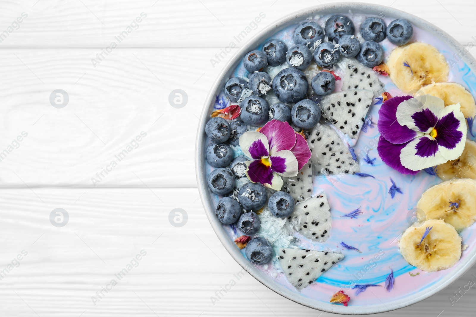 Photo of Delicious smoothie bowl with fresh fruits, blueberries and flowers on white wooden table, top view. Space for text