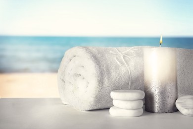 Image of Towel, spa stones and candle on table against seascape