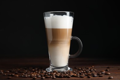 Photo of Delicious latte macchiato and coffee beans on wooden table