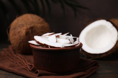 Coconut pieces in bowl and nuts on wooden table