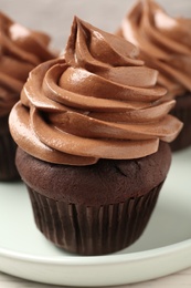 Photo of Delicious fresh chocolate cupcake with cream on plate, closeup