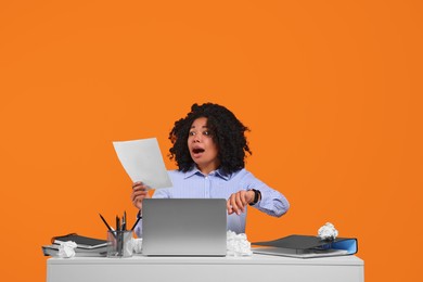 Stressful deadline. Scared woman looking at document at white desk against orange background