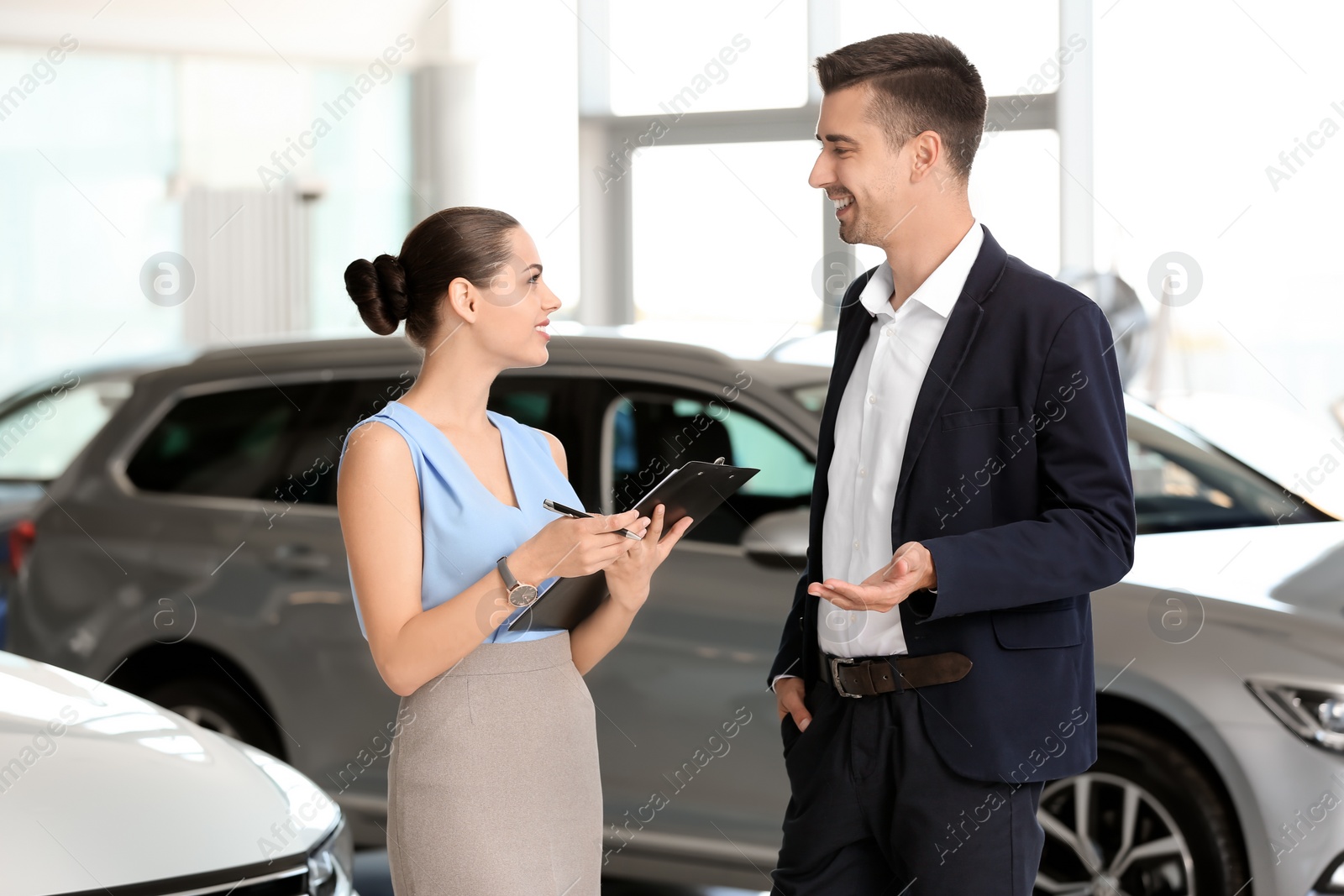 Photo of Young saleswoman working with client in car dealership