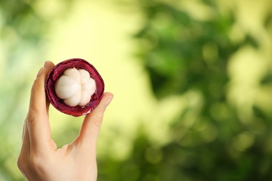 Photo of Woman holding open mangosteen fruit outdoors, closeup. Space for text