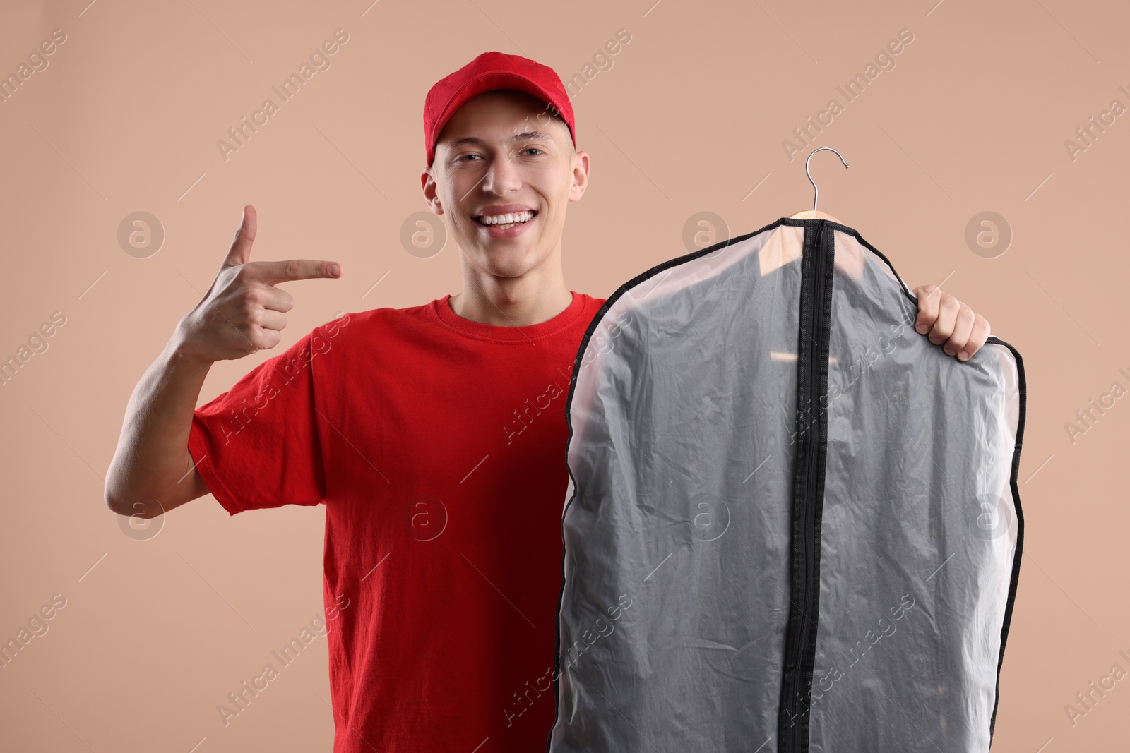 Photo of Dry-cleaning delivery. Happy courier holding garment cover with clothes on beige background