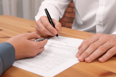 Businesspeople signing contract at wooden table in office, closeup of hands