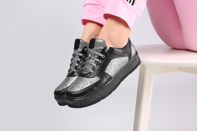 Photo of Woman in stylish sport shoes sitting on stool against light background