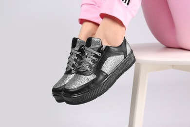 Woman in stylish sport shoes sitting on stool against light background