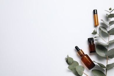 Aromatherapy. Bottles of essential oil and eucalyptus branches on white background, flat lay. Space for text