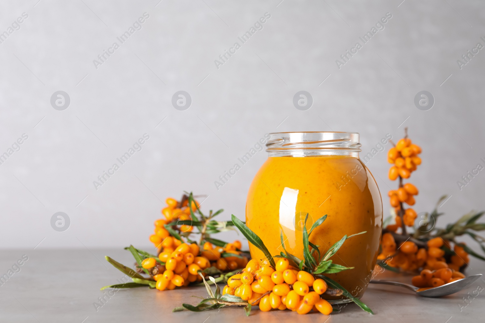 Photo of Delicious sea buckthorn jam and fresh berries on grey table. Space for text