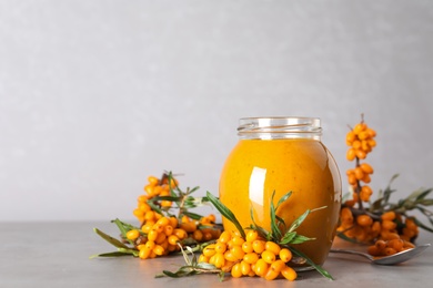 Delicious sea buckthorn jam and fresh berries on grey table. Space for text