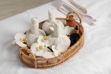 Photo of Wicker tray with herbal bags and other spa products on white bath towel