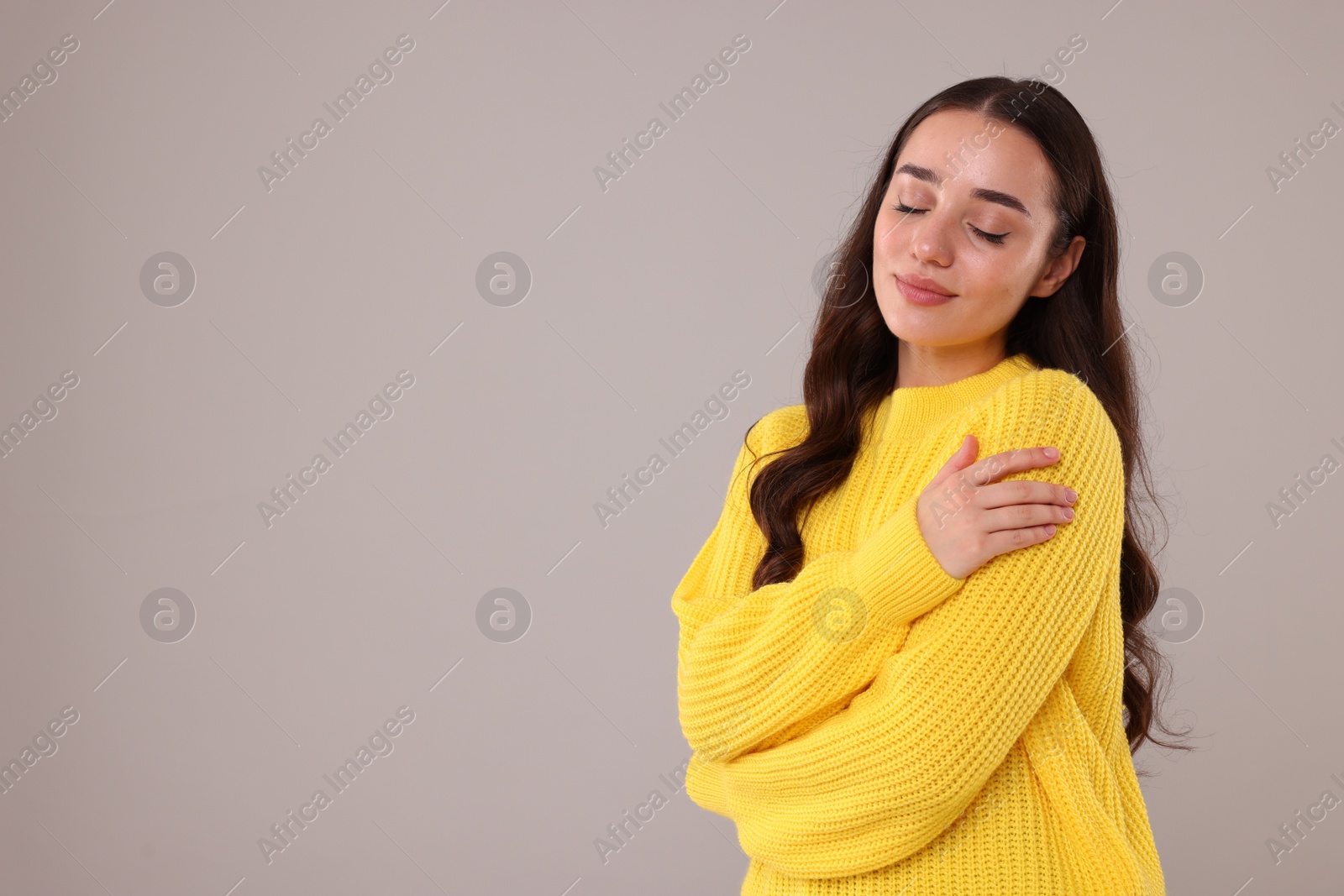 Photo of Beautiful young woman in stylish warm sweater on grey background, space for text