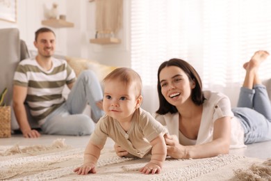 Happy parents helping their cute baby to crawl on floor at home