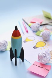 Photo of Composition with toy rocket and stationery on light blue background. Startup concept