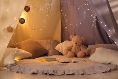 Photo of Play tent with books, pillows and Teddy bear. Modern children's room interior