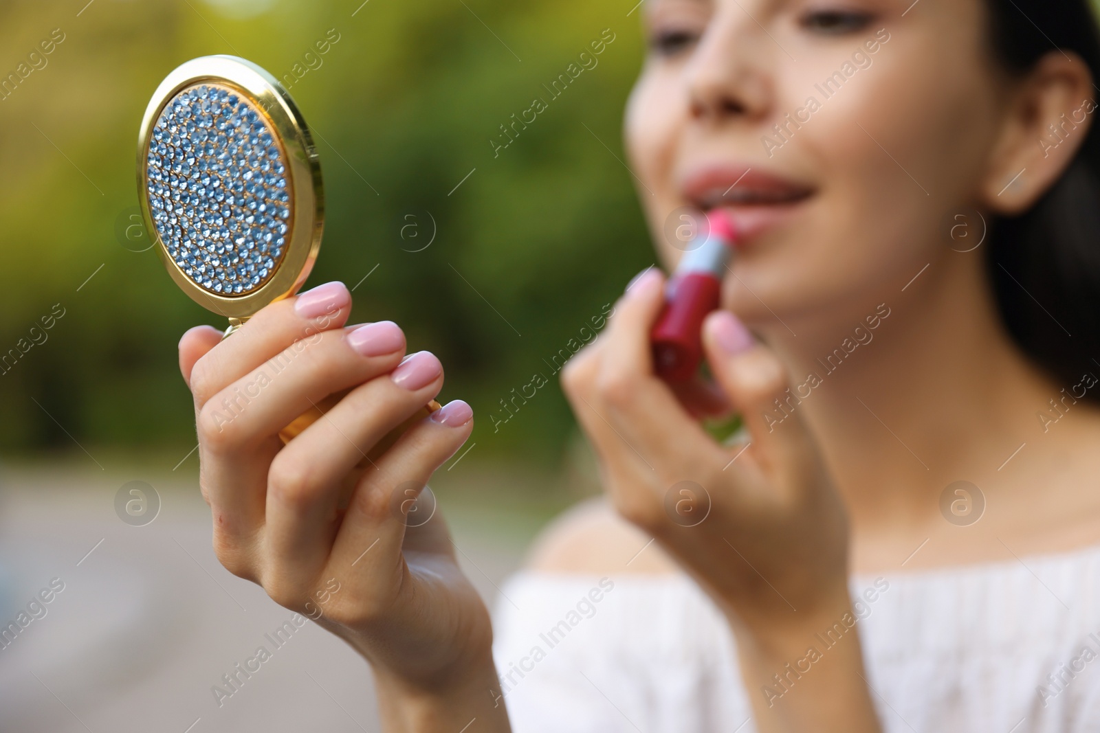 Photo of Woman with cosmetic pocket mirror applying lipstick outdoors, closeup