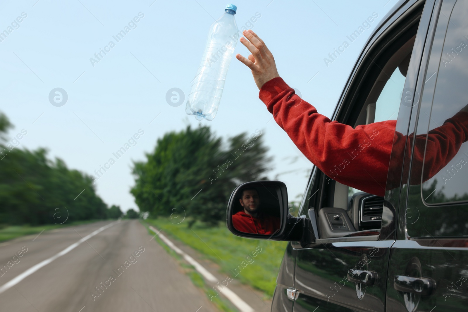 Photo of Driver throwing away plastic bottle from car window. Garbage on road