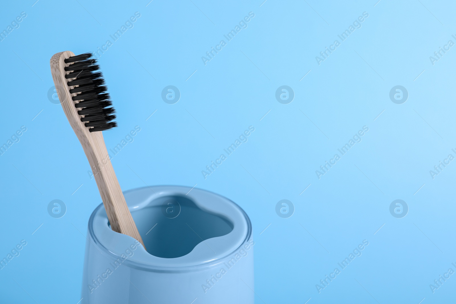Photo of Bamboo toothbrush in holder on light blue background, space for text
