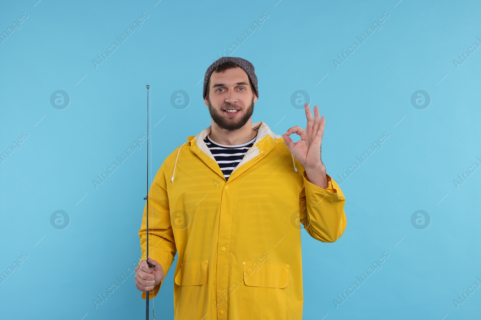 Photo of Fisherman with fishing rod showing ok gesture on light blue background