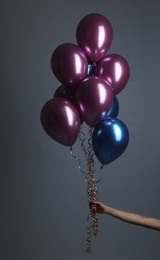 Woman holding bunch of balloons on grey background, closeup