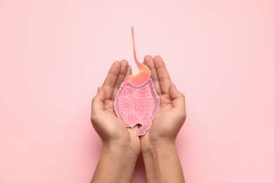 Photo of Woman holding paper cutout of small intestine on pink background, top view