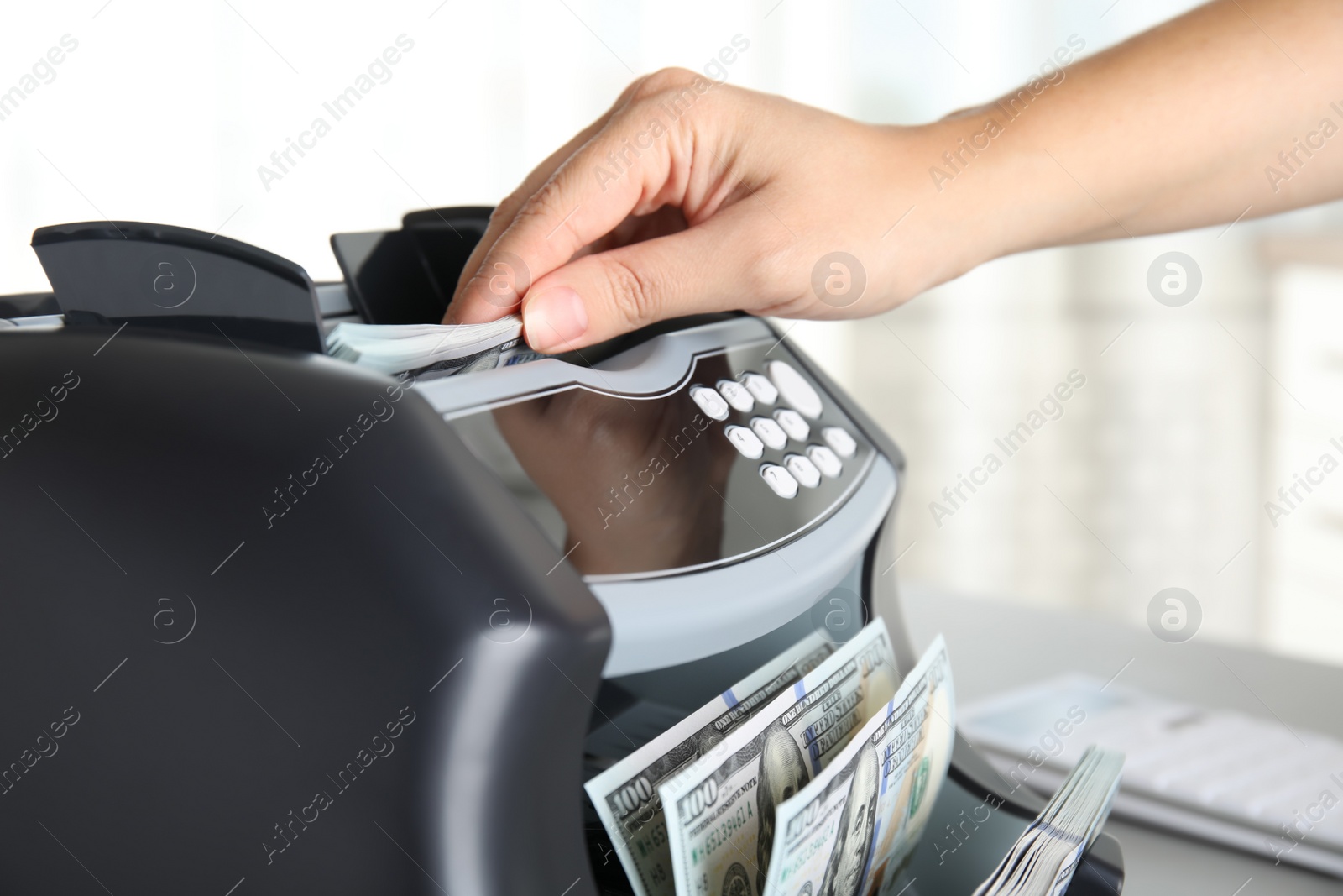 Photo of Woman putting money into counting machine at table indoors, closeup