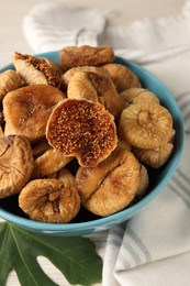 Photo of Bowl with tasty dried figs and green leaf on table, closeup